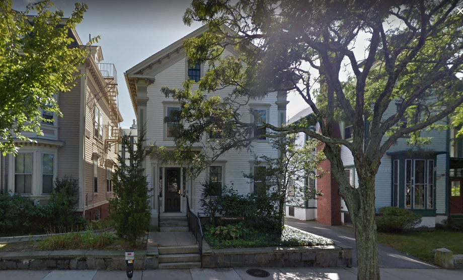 a white house on a densely packed residential street with trees and shrubs