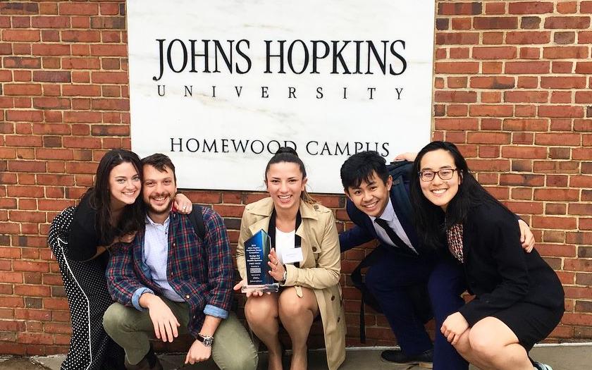 Team of Brown and RISD students posing in front of Johns Hopkins sign