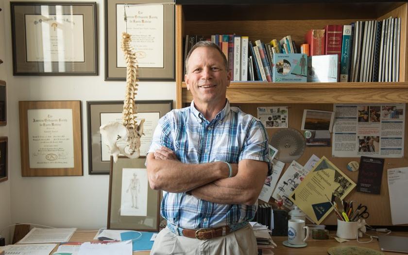 J.J. Trey Crisco smiling for a portrait in his office, in front of a model spine and bookshelf