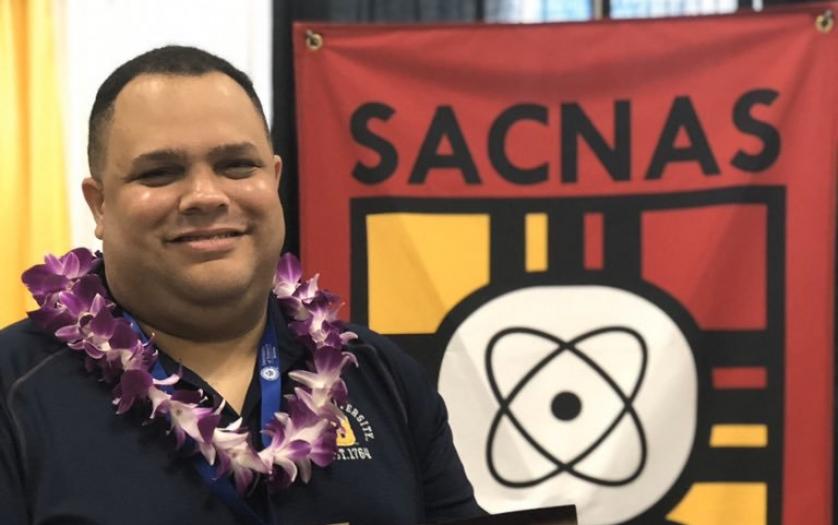Rafael Gonzalez-Cruz stands in front of the SCNAS flag with a lei on