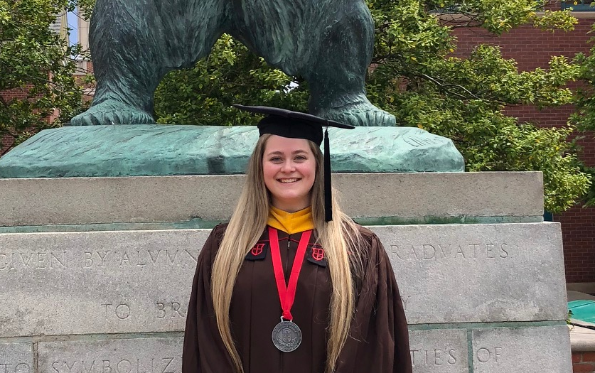 Deanna Stueber stands in front of a Bear Statue in a graduation robe