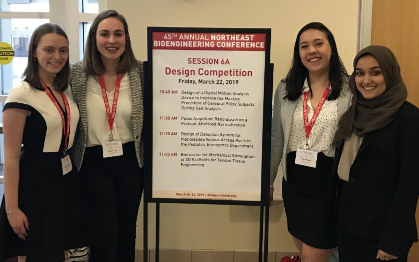 Four students wearing lanyards around a conference sign
