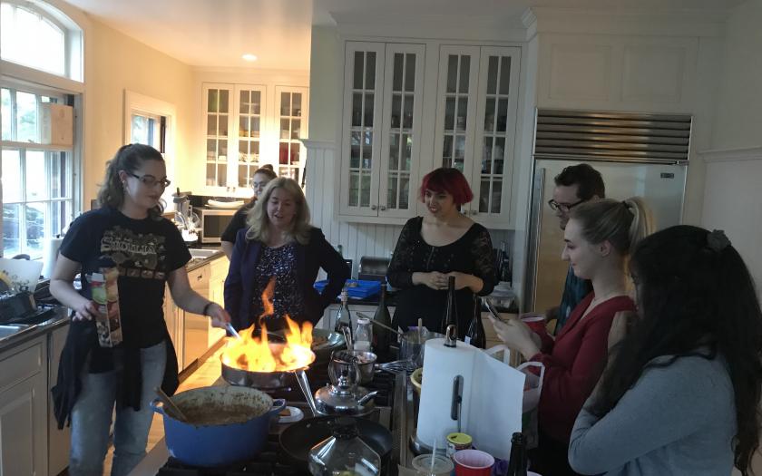 Faculty and students stand in a kitchen around a stove watching a fire flaring in a pan