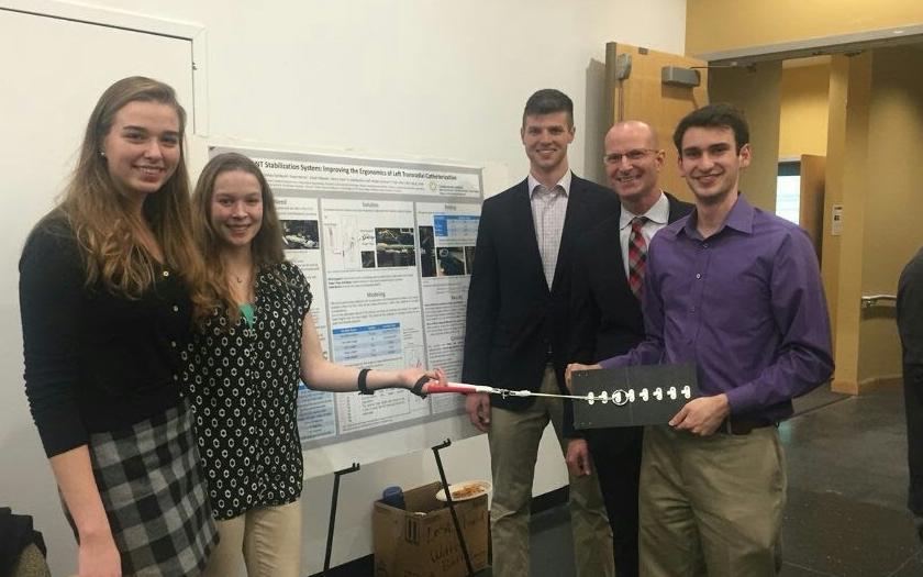 Students stand in front of a research presentation poster smiling and demonstrating a design