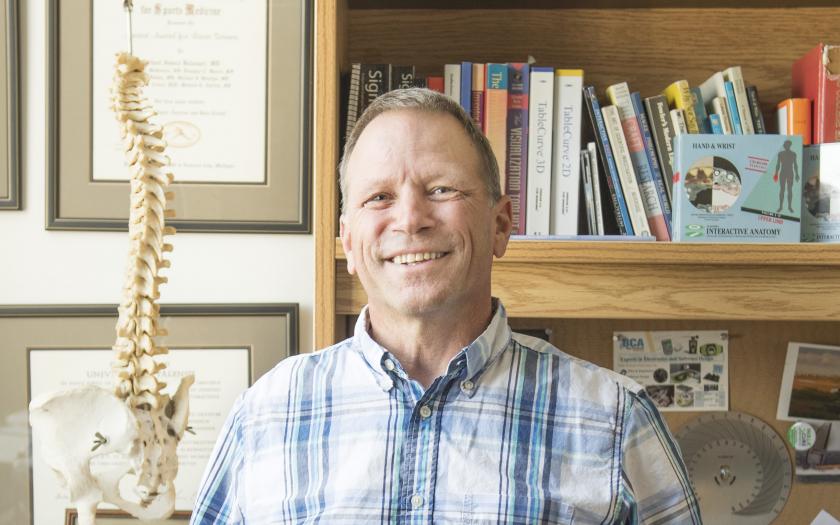 J.J. Trey Crisco smiling for a portrait in his office, in front of a model spine and bookshelf