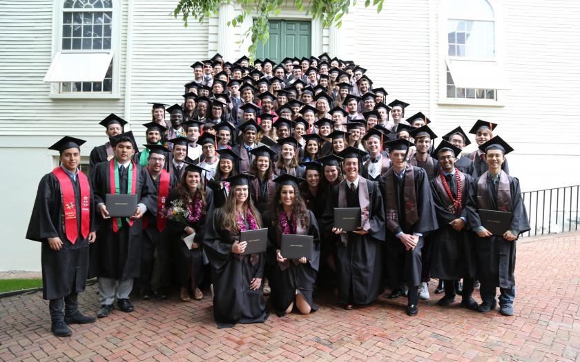 50 students wearing graduation gowns in front of a white building