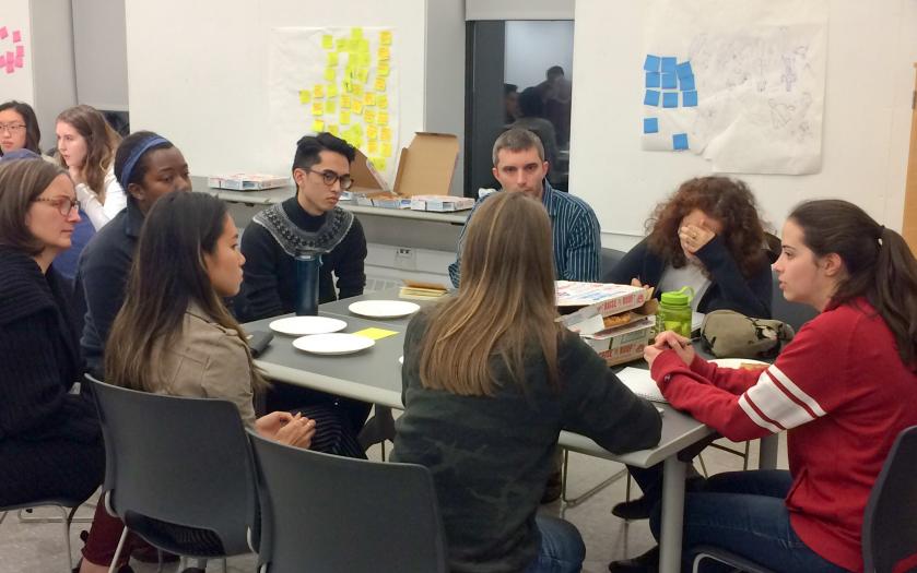 Students sit around a table around pizza and posters