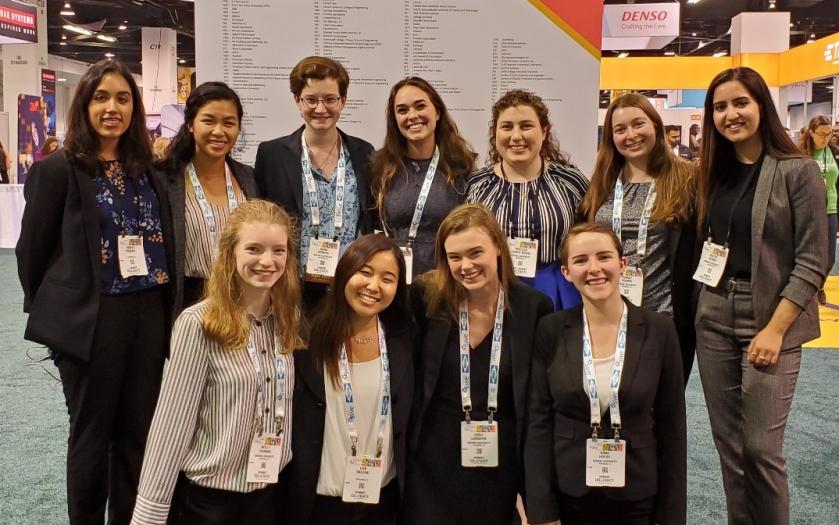 Women in professional attire and lanyards take a group photo at a conference