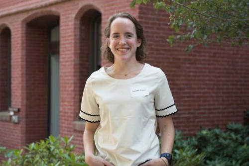 waist up portrait of a young adult outside in front of a brick building wearing a white shirt.